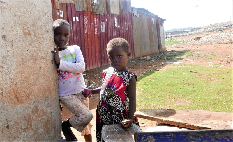 Nágrannabörn Labans og Scoviu við hús þeirra hjóna. Öskuhaugar að baki barnanna. Mynd: Sunna Ósk Logadóttir