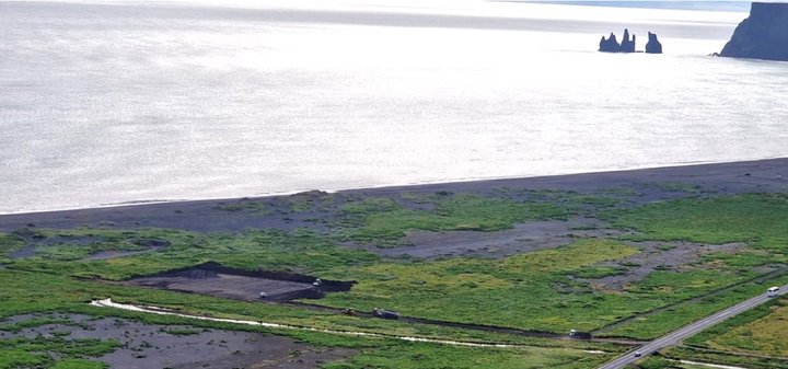 Horft yfir vinnslusvæði Lavaconcept ofan af Fagradalshamri. Myndin er tekin á framkvæmdatíma þegar unnið var að jarðvinnu. Svæðið er rétt við þjóðveg 1 í lúpínubreiðu austan við Vík, Reynisdrangar sjást í fjarska.