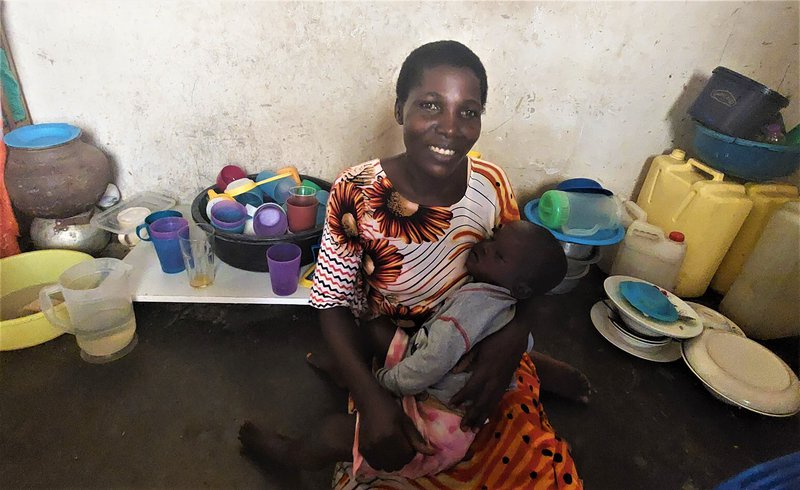 Scovia með Lars sofandi í fanginu. Hún situr í horninu þar sem hún eldar. Lengst til hægri er heimatilbúinn kælir.Mynd: Sunna Ósk Logadóttir