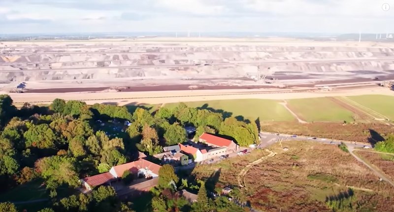 Síðasti bærinn í dalnum. Honum á að fórna, ásamt litla þorpinu í kring. Efst á myndinni má sjá námuna gríðarstóru. Skjáskot: YouTube