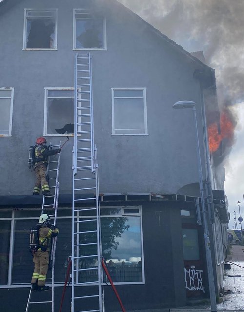 Eldtungur út um gluggann á herberginu á 2. hæðinni sem kveikt var í og slökkviliðsmenn að störfum á norðurhlið hússins. Mynd: Aðsend
