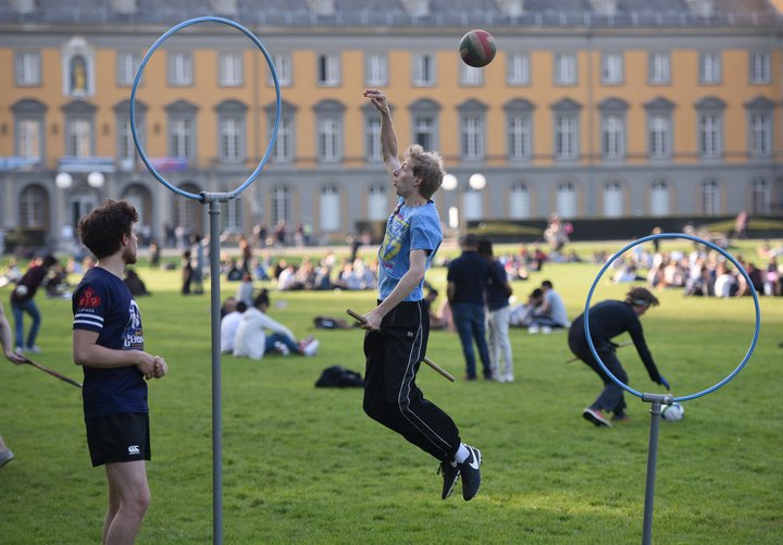 Quadball iðkendur með kústsköft á milli lappanna. Gjarðirnar í forgrunni er mörkin, hægt er að vinna sér inn stig með því að koma tromlunni inn fyrir mark andstæðingsins.