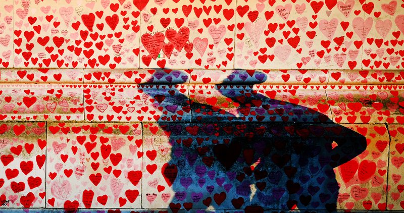 Skuggar vegfarenda falla á minningarvegg um þá sem látist hafa úr COVID-19 í London. Mynd: EPA