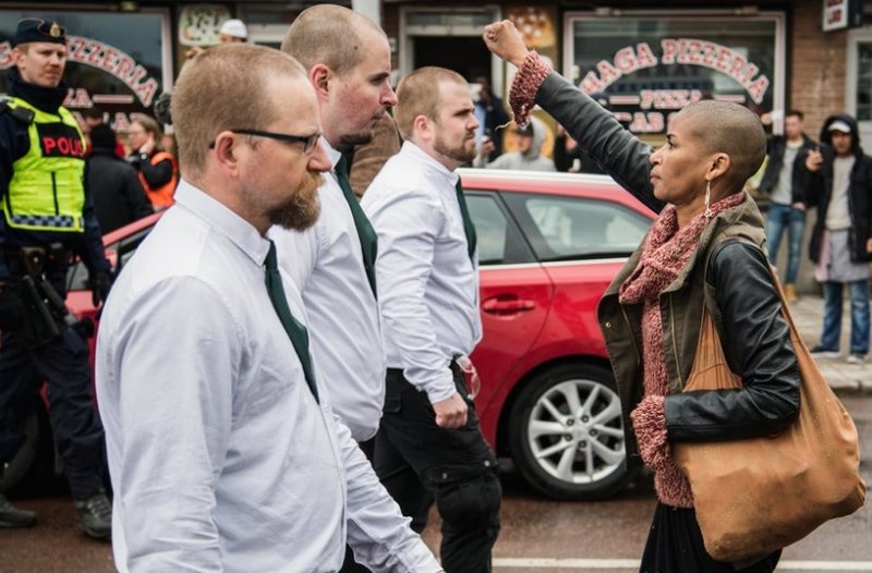 Ungir menn, sem aðhyllast rasisma, í Svíþjóð, labba fram á svarta konu sem lætur ekki fordómafulla rasista ganga um með boðskap sinn í friði. Mynd: EPA.